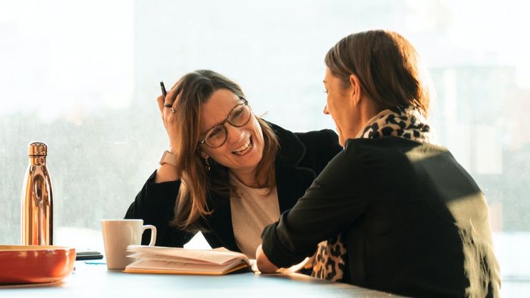 Two women in business meeting sitting at table talking to each other and smiling